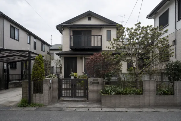 曇り空の下の、日本の住宅街に建つ2階建ての一戸建て。門扉と前庭が見える